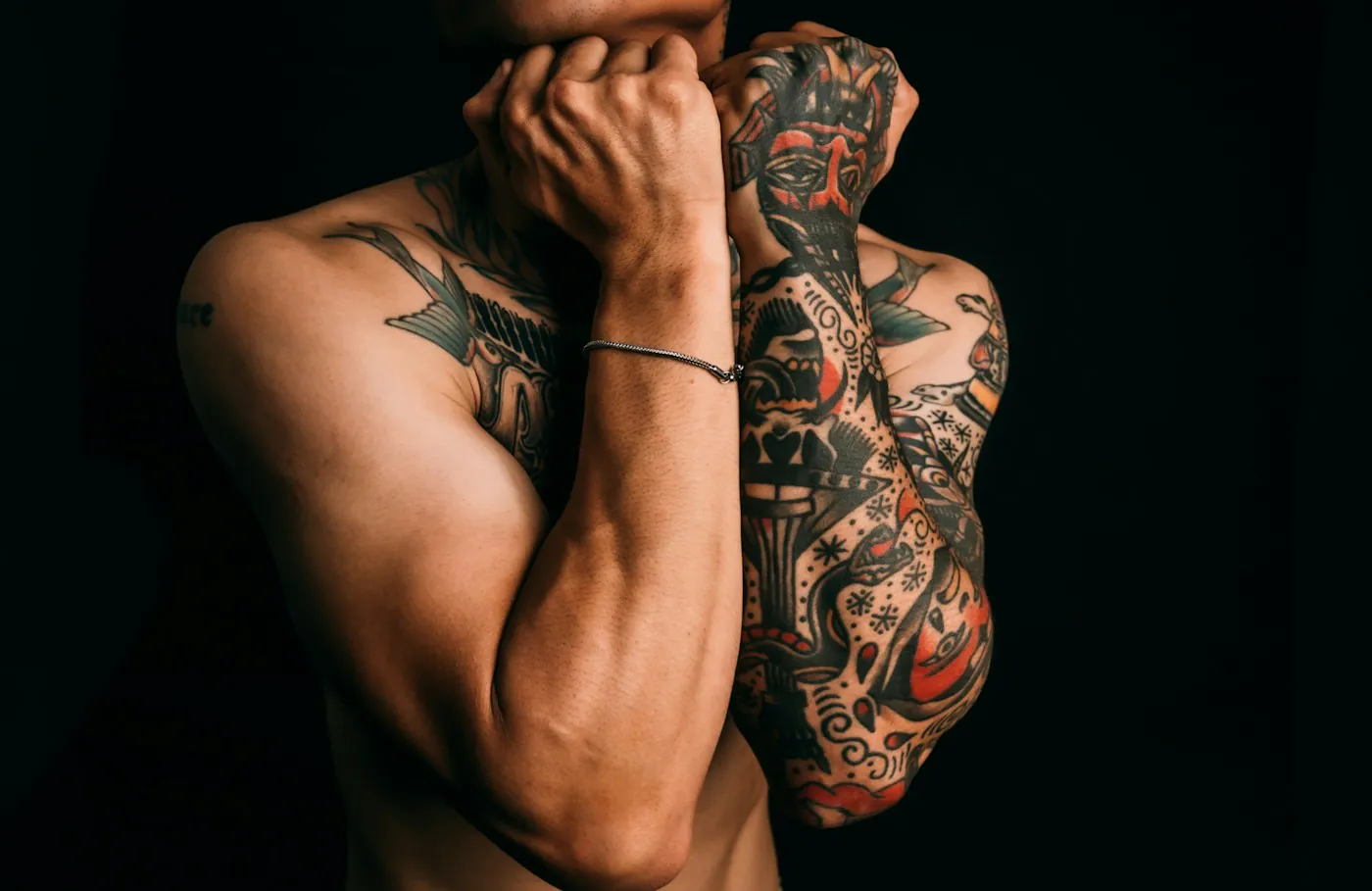 Uomo con entrambe le braccia tatuate su fondo nero