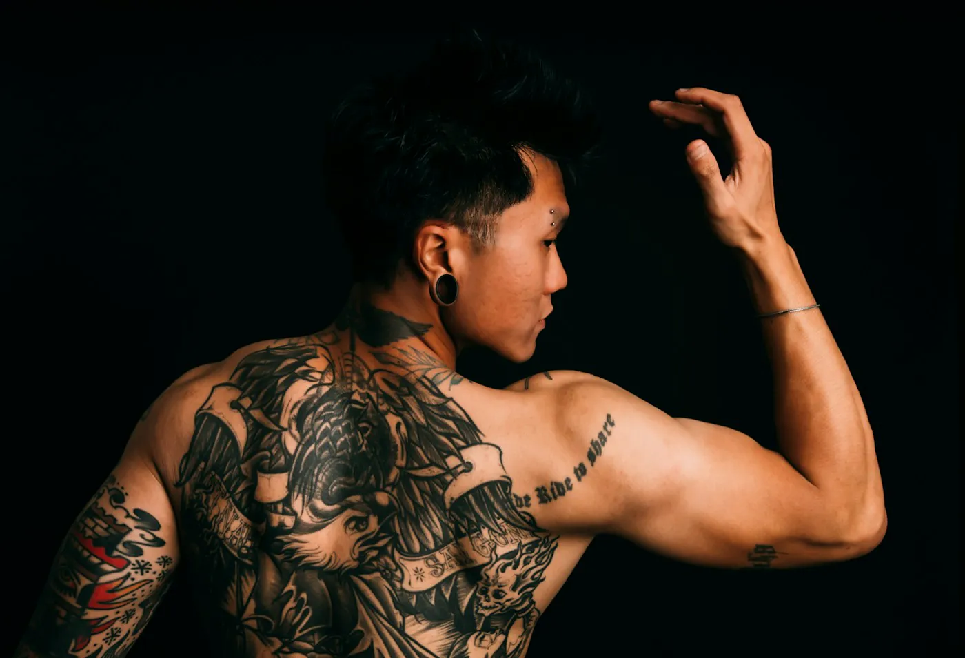Ragazzo di spalle con schiena tatuata, luce bassa