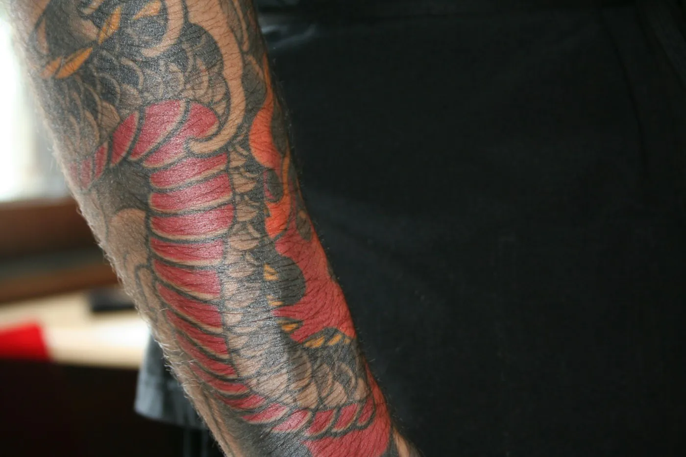 Braccio con drago rosso e onde tatuati