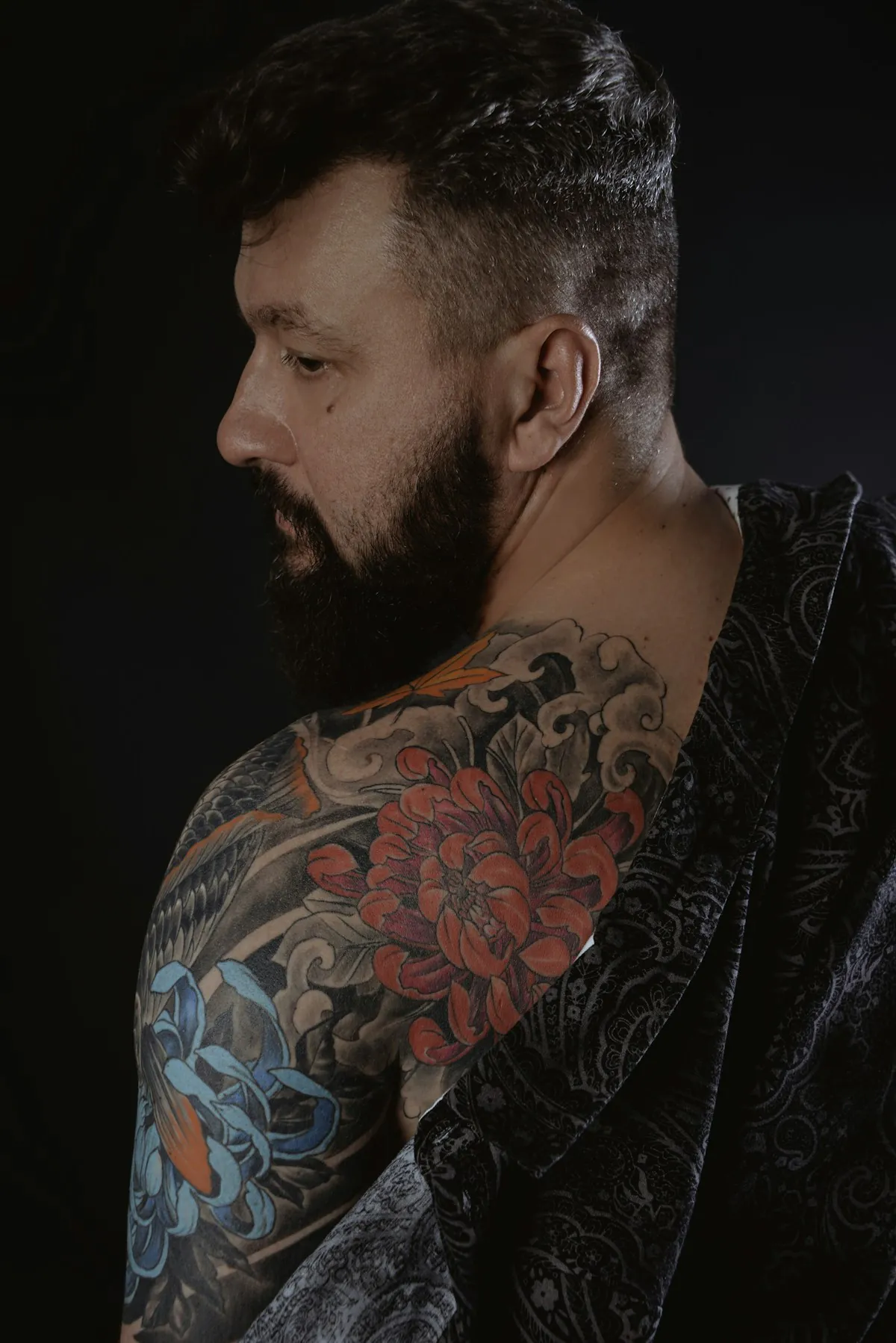 Uomo con la barba e manica tatuata a colori con peonie